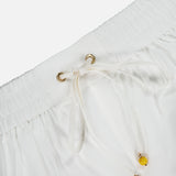 Close-up of the Mahon Embroidered Drawstring Short by ZIMMERMANN, showcasing an ivory high-rise fit with gold eyelets, yellow bead-accented drawstrings, and an elastic gathered waistband for comfort and style.