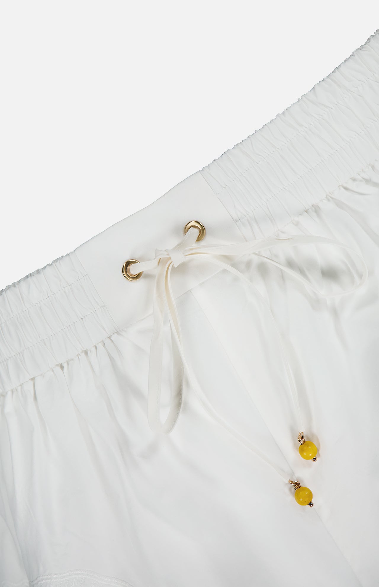 Close-up of the Mahon Embroidered Drawstring Short by ZIMMERMANN, showcasing an ivory high-rise fit with gold eyelets, yellow bead-accented drawstrings, and an elastic gathered waistband for comfort and style.