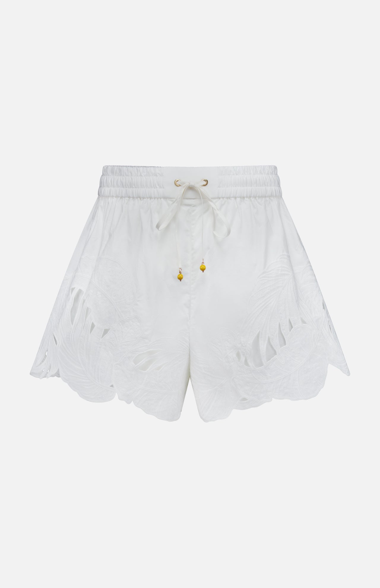 The ZIMMERMANN Mahon Embroidered Drawstring Short features an ivory hue, gold bead accents, and leaf-patterned cutouts along the scalloped hem. Made from cotton, these high-rise shorts are shown against a plain white background.