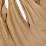 Close-up of light brown, silky fabric from the ZIMMERMANN Mahon Shell Charms Maxi Dress, gathered with gold chain links and delicate seashell charms for luxurious folds and elegant texture.