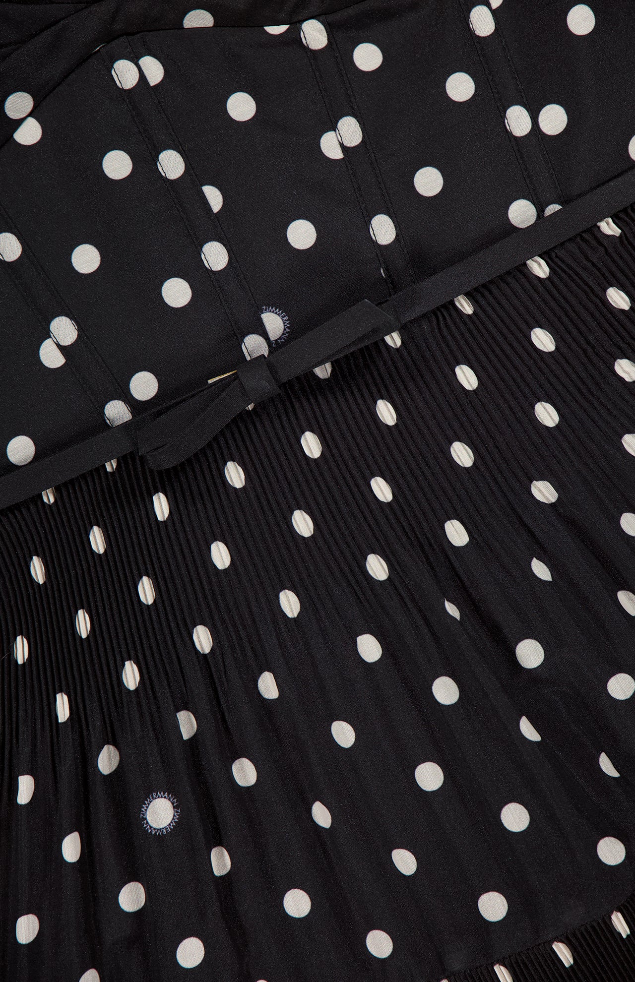 Close-up of the ZIMMERMANN Pleated Draped Mini Dress, featuring black polka dot fabric with smooth and pleated textures, highlighting its detailed stitching and chic party-ready design.