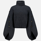The Valiant Buttoned Sweater by ZIMMERMANN is a dark gray cropped turtleneck with a high neckline and wide, balloon sleeves adorned with button details along the outer seams. Displayed against a plain white background, this statement piece blends modern design and cozy comfort—making it an eye-catching addition to your sweater collection.