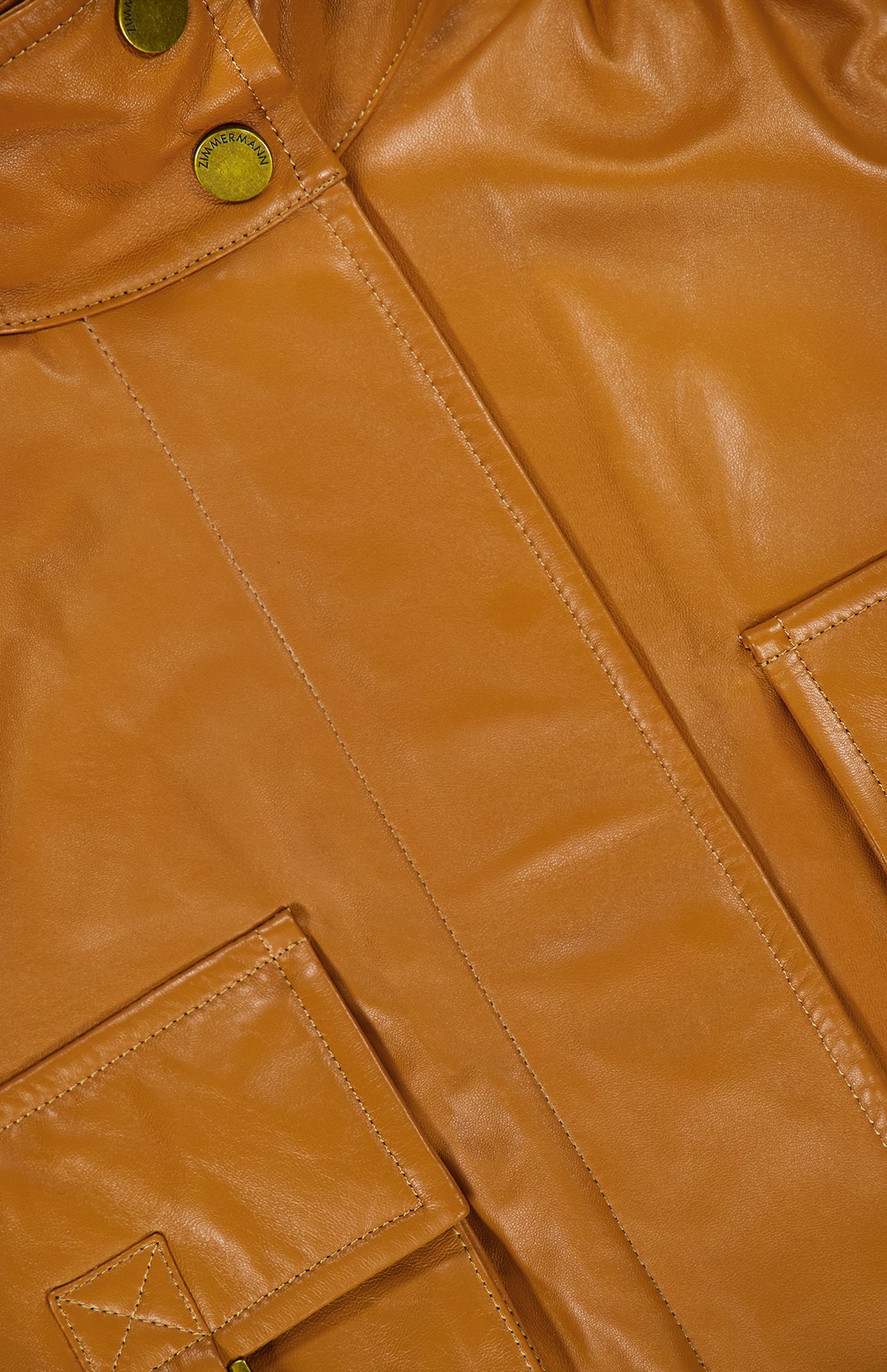Close-up of a Zimmermann Valiant Leather Biker Jacket in amber, featuring a collar with brass-toned snap buttons and two large flap pockets.