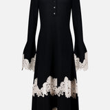 The Valiant Merino Lace Dress by ZIMMERMANN is a black merino wool midi dress featuring a collared neckline, buttoned front, and a graceful flared skirt, elegantly finished with beige lace-embroidered trim on the cuffs, hem, and near the lower skirt.