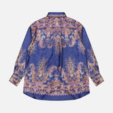 The ZIMMERMANN Valiant Relaxed Bow Collar Shirt is a designer women’s long-sleeve button-up, featuring a blue base adorned with intricate gold, pink, and purple paisley patterns, shown from the back against a plain white background.