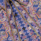 A close-up of the ZIMMERMANN Valiant Relaxed Bow Collar Shirt, featuring a richly patterned blue and gold silk paisley design with ornate buttons, tie details, and the designer’s label on the collar—capturing the essence of this luxurious women’s shirt.
