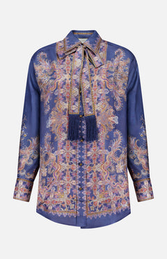 The ZIMMERMANN Valiant Relaxed Bow Collar Shirt is a long-sleeve, button-up silk blouse in deep blue, featuring an ornate gold and pink paisley pattern and a matching bow collar necktie embellished with fringed tassels—offering the perfect blend of designer women’s shirt elegance and subtle bohemian charm.