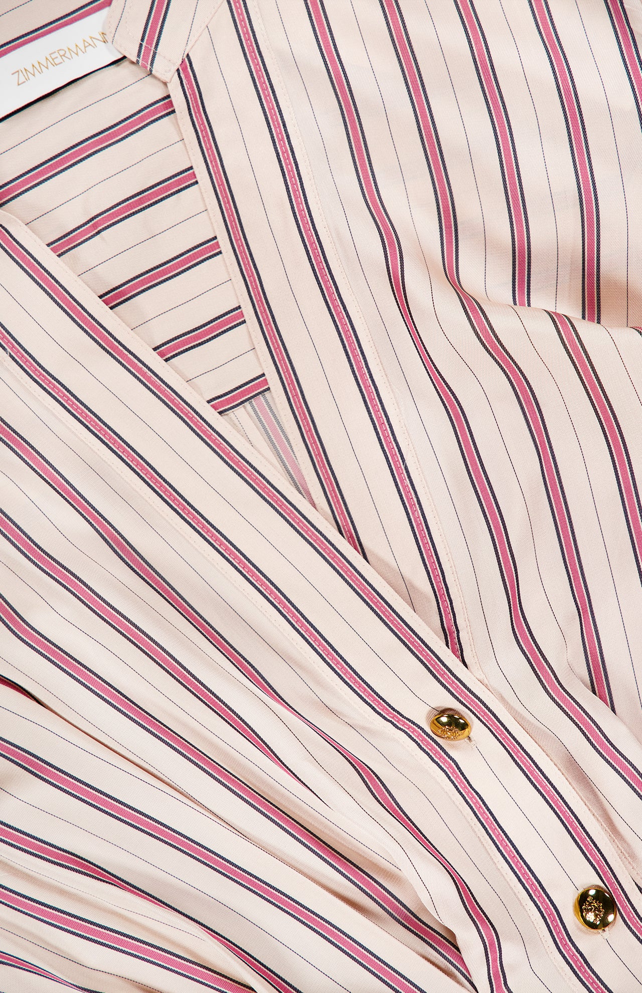 Close-up of the ZIMMERMANN Valiant Tuck Striped Shirt Dress, featuring cream-colored fabric with vertical red and navy blue stripes, gold buttons, and a visible brand label in the top left corner.