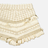 The Wanderlust Crochet Short by ZIMMERMANN features a beige, textured design with scalloped hems, decorative patterns, and layered ruffles along the legs and waistband.
