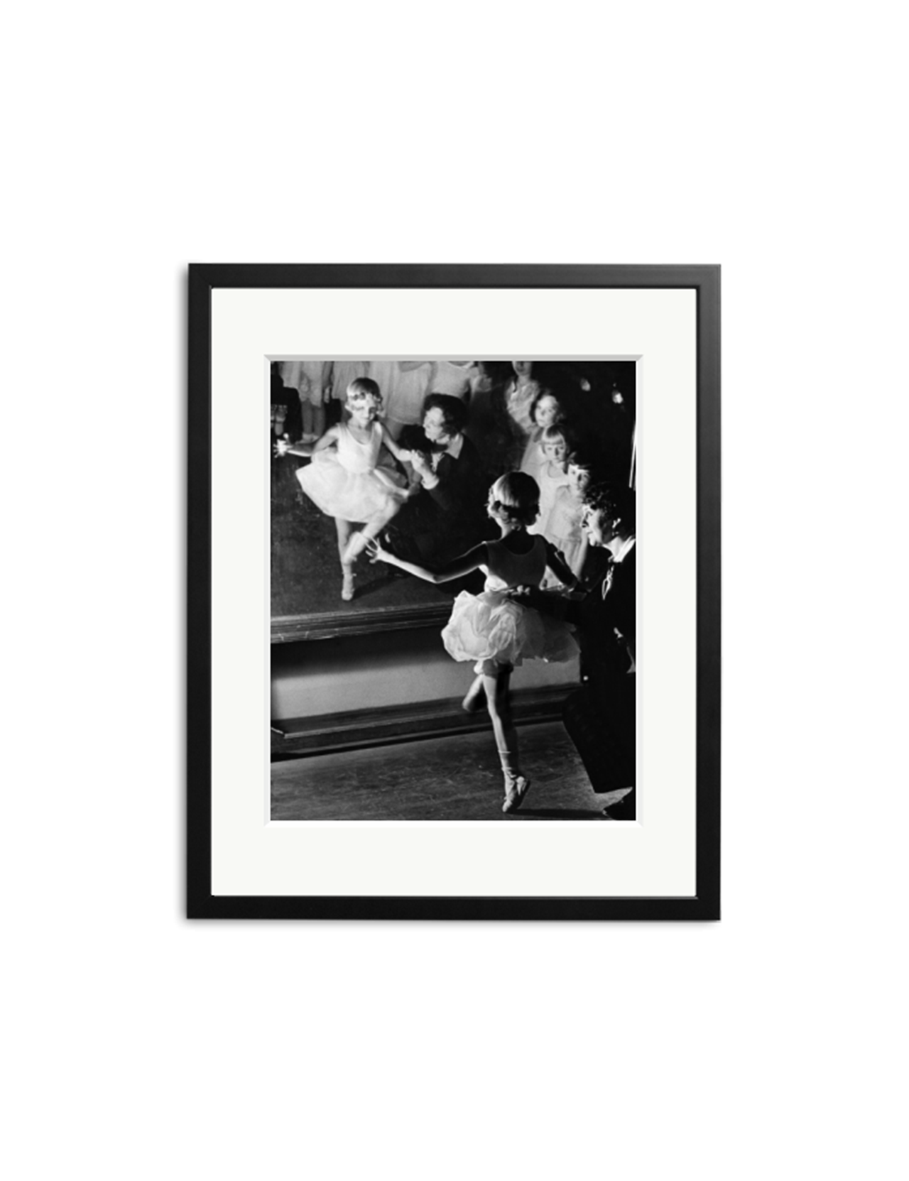 “Ballet Girls” by SONIC EDITIONS is a black and white photo of a young ballerina with her teacher, both reflected in a mirror. Elegantly presented in a simple black frame with a white mat.