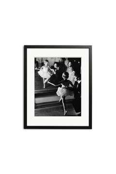 “Ballet Girls” by SONIC EDITIONS is a black and white photo of a young ballerina with her teacher, both reflected in a mirror. Elegantly presented in a simple black frame with a white mat.