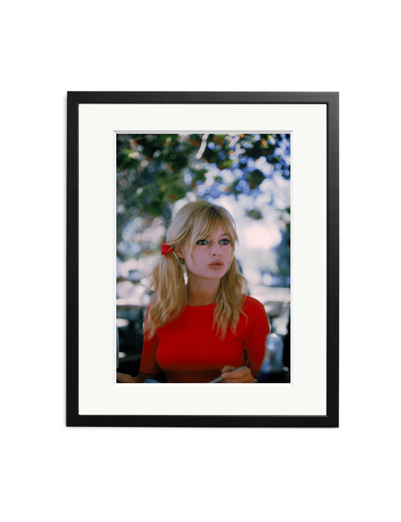 Brigitte Bardot on Set" by SONIC EDITIONS is a framed photograph capturing the iconic star with blonde pigtails in a red top, seated outdoors among blurred green foliage and sunlight—a stunning limited edition artwork.