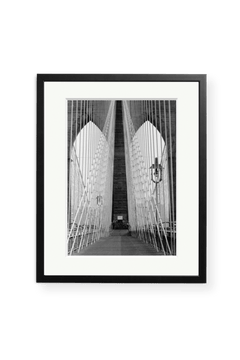 The "Brooklyn Bridge Walkway" by SONIC EDITIONS is a black and white photo of the iconic bridge, featuring cables and arches, offered as limited edition framed wall art in a sleek black frame with a white mat.