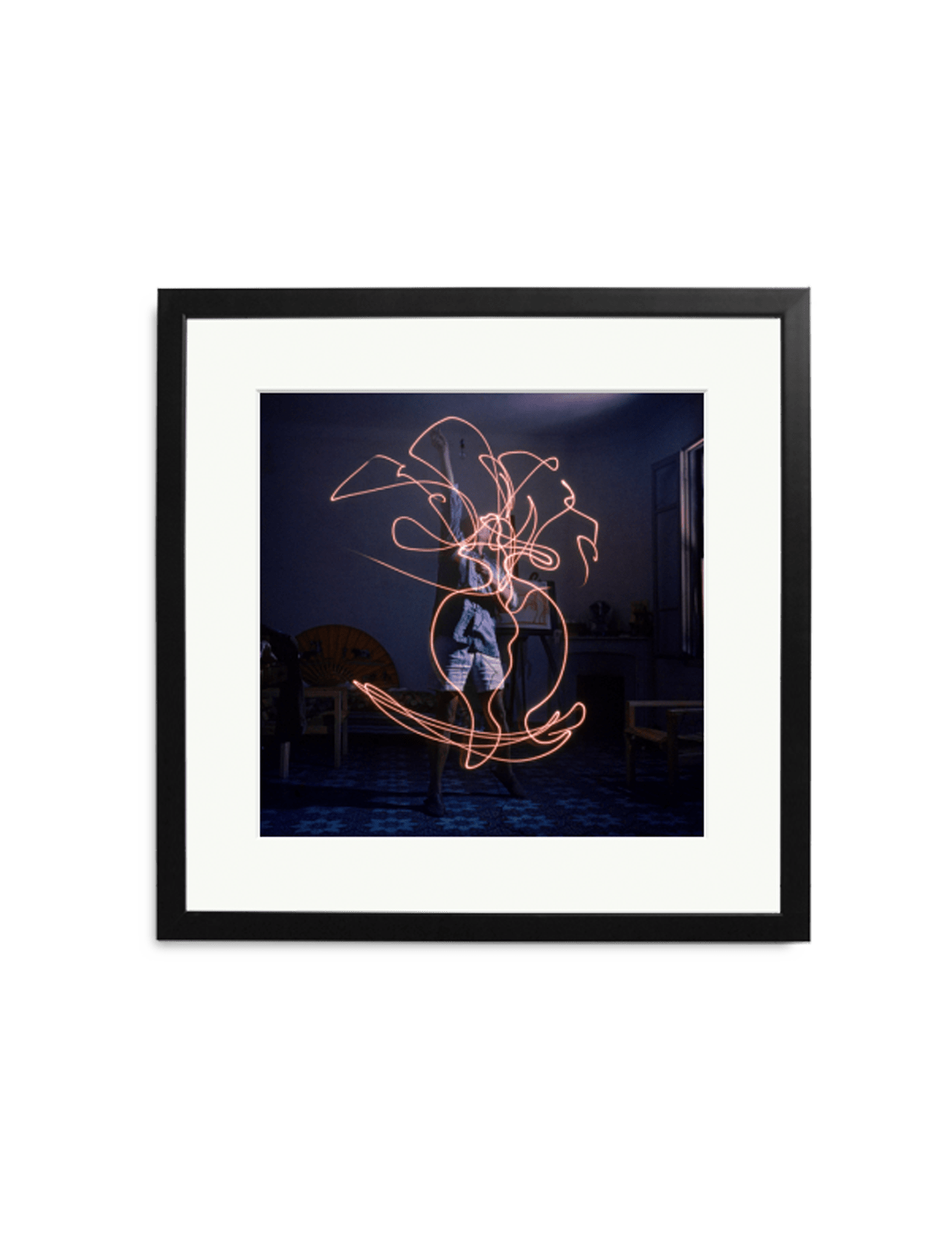 Discover a limited edition: SONIC EDITIONS' "Picasso Light Drawing, 1949"—a striking framed photo capturing Picasso in a dim room with swirling orange light trails, furniture, and a window adding depth to this unique wall decor.