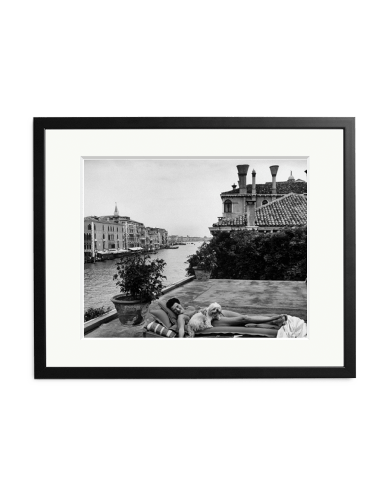 Black-and-white Peggy Guggenheim print by SONIC EDITIONS shows a person and dog relaxing on a rooftop terrace overlooking a river and historic buildings, framed with a white mat and black frame.